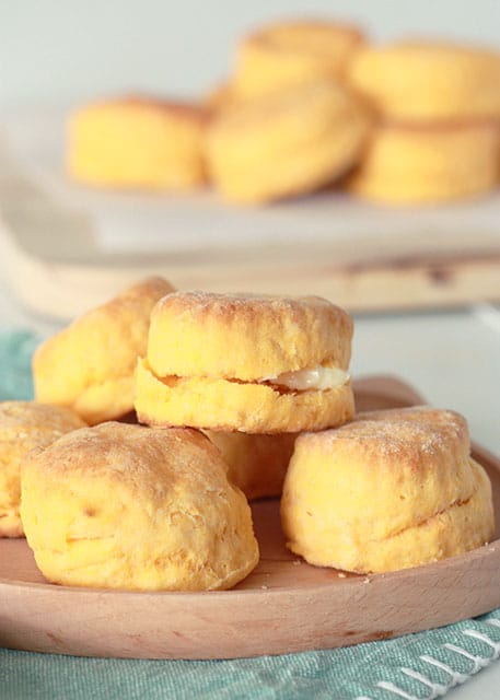 sweet potato biscuits on a wooden plate stacked with sweet potato biscuits in background